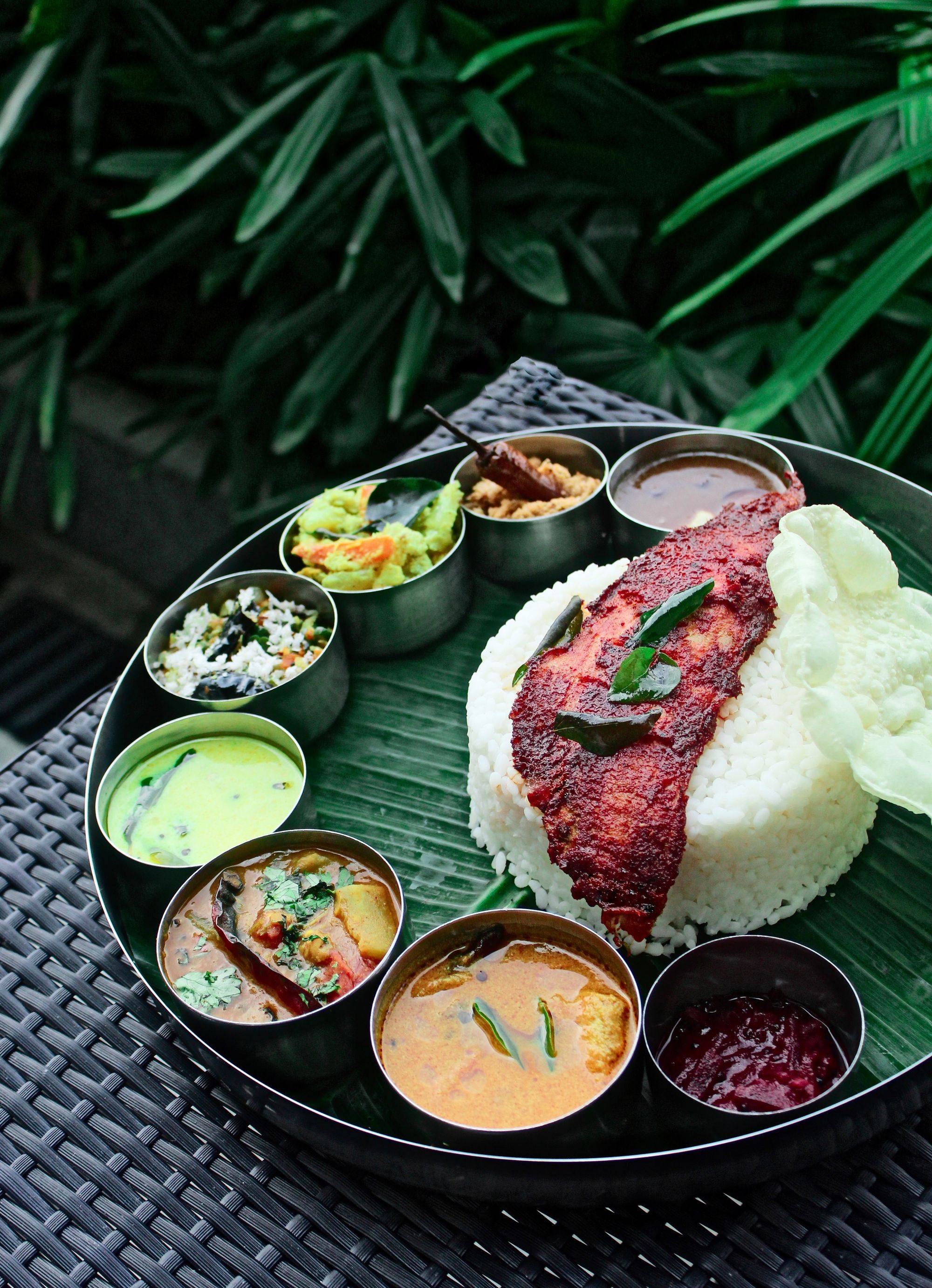 A Kerala meal on a banana leaf: red fried fish on rice with pappadam, ringed by small bowls of curry